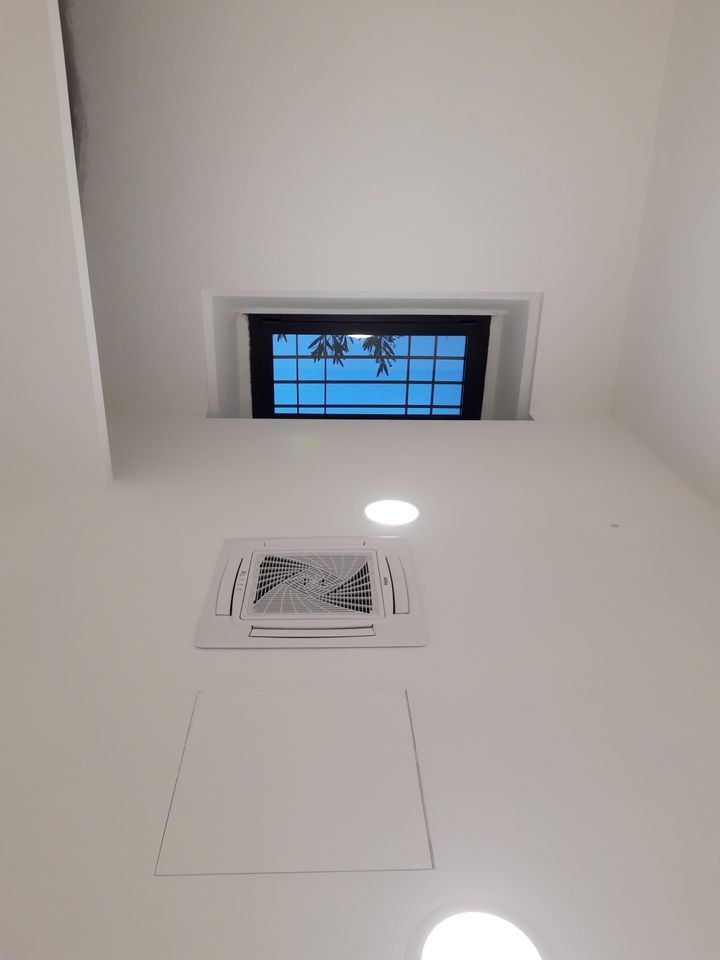 White suspended ceiling with spotlights, air-conditioning unit and inspection hatch, next to a high window