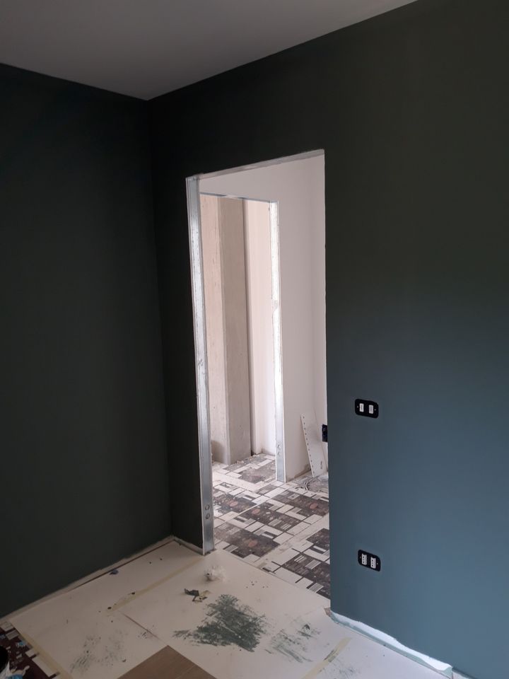 Room with walls painted dark petrol green and a doorway to the next room, floor still protected