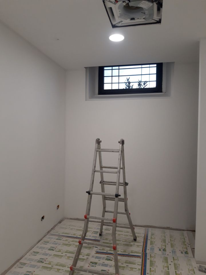 Room painted white with a high window, ladder and floor still protected